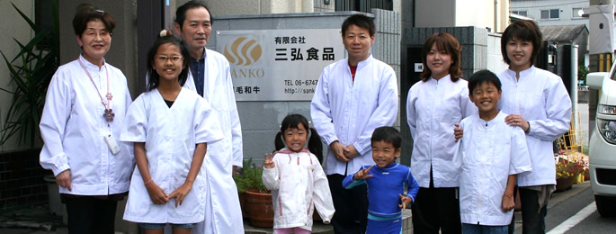 三弘食品の看板の前で、白衣のスタッフと家族